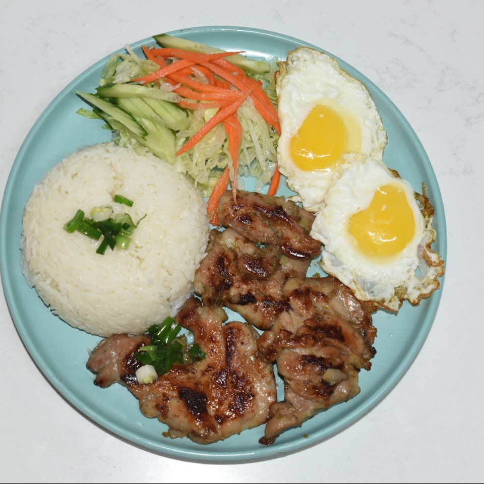Grilled pork with rice, two fried eggs, and shredded cucumber-carrot salad on a turquoise plate.